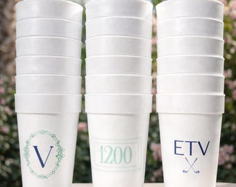 May include: White disposable cups stacked in three columns. Each cup has a decorative design or text in blue or teal. One cup has the letter "V" inside a floral design. Another has the number "1200". The third has the letters "ETV" and crossed golf clubs.