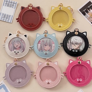 Könnte beinhalten: Eine Sammlung von katzförmigen Ausweishaltern in verschiedenen Farben, darunter Rot, Gelb, Weiß, Hellblau, Schwarz, Lila, Rosa und Fuchsia. Jeder Halter hat ein klares Fenster für eine Karte oder ein Foto und einen goldfarbenen Schlüsselanhänger.