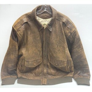 May include: A brown leather bomber jacket with a collared neckline and two front pockets. The jacket has a ribbed hem and cuffs. The leather has a distressed appearance, with variations in color and texture. The jacket is hanging on a clear hanger.