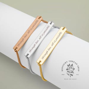 May include: Three bar bracelets in rose gold, silver, and gold, each engraved with "through love, all is possible." The bracelets are connected to delicate chain links. The Midnight Thread Shop logo is visible.