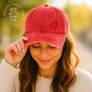 May include: Red baseball cap with a curved brim and a small embroidered design on the front. The cap has a distressed look and a six-panel design. The Midnight Thread Shop logo is visible on the side.