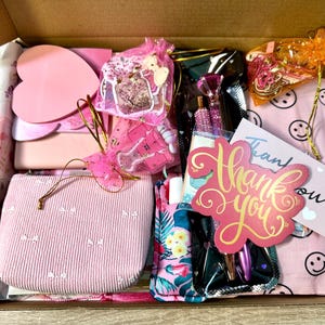 Pu&ograve; includere: Una scatola regalo in cartone riempita di articoli di cancelleria e accessori, tra cui una pochette in velluto a coste rosa, foglietti adesivi a forma di cuore, un astuccio a fiori, penne con tappi a diamante, un biglietto di ringraziamento e sacchetti.