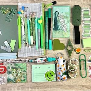 May include: A collection of green-themed stationery including a notebook, pens, pencils, markers, paper clips, sticky notes, bookmarks, and various stickers. The items feature floral, book-related, and smiley face designs, with some labeled as book reviews.