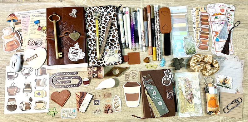 May include: A collection of stationery items including two leather-bound journals, a leopard print pencil case, various pens, markers, and highlighters. Also included are decorative stickers, bookmarks, a gold key, a scrunchie, and paper clips.