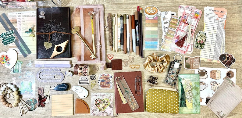 May include: A collection of stationery items including a dark leather journal, a brown notebook, various pens, pencils, markers, a mesh pencil case, a gold key-shaped pen, a gold scrunchie, a polka dot pouch, bookmarks, stickers, and reading lists.