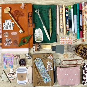 May include: A collection of stationery items including two notebooks, various pens, markers, bookmarks, stickers, a small pouch, a scrunchie, and paper clips. The items feature coffee-themed designs, floral patterns, and motivational text.