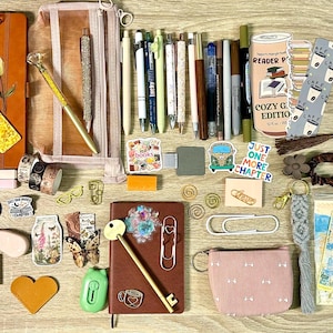 May include: A collection of stationery and reading accessories including two notebooks, a pencil case, various pens, bookmarks, stickers, paper clips, a small pouch, and reading lists. The items feature diverse colours, patterns, and text like 'Just one more chapter'.