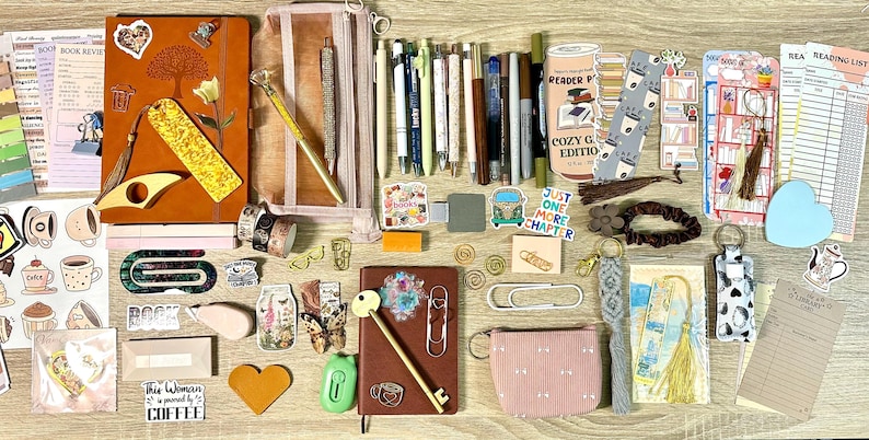 May include: A collection of stationery and reading accessories including two notebooks, a pencil case, various pens, bookmarks, stickers, paper clips, a small pouch, and reading lists. The items feature diverse colours, patterns, and text like 'Just one more chapter'.