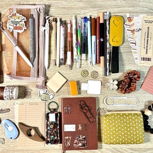 May include: A collection of stationery items including two notebooks, a mesh pencil case, various pens, markers, and pencils. Also included are bookmarks, stickers, paper clips, sticky notes, a small yellow polka dot pouch, and printed book review forms.