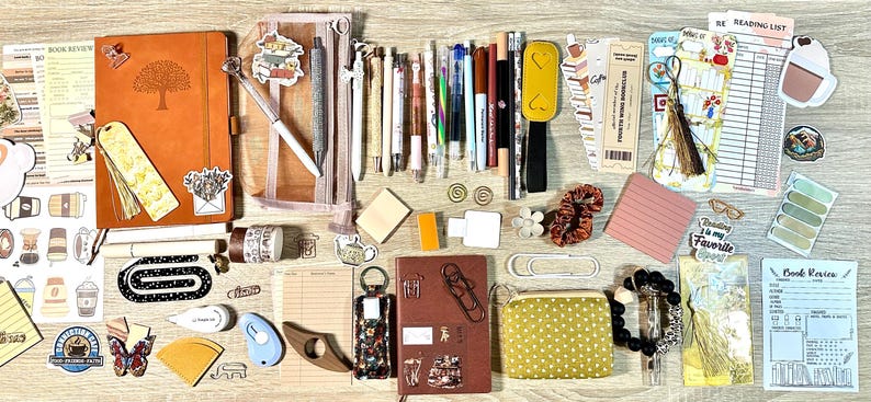 May include: A collection of stationery items including two notebooks, a mesh pencil case, various pens, markers, and pencils. Also included are bookmarks, stickers, paper clips, sticky notes, a small yellow polka dot pouch, and printed book review forms.