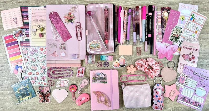 Pu&ograve; includere: Una collezione di articoli di cancelleria rosa che include due quaderni, un astuccio, varie penne, pennarelli, graffette, foglietti adesivi, segnalibri, una piccola pochette, un elastico per capelli e adesivi decorativi con motivi floreali, farfalle e libri.