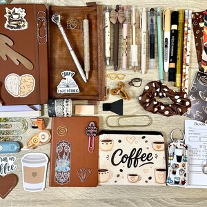 May include: A collection of stationery items including two brown notebooks, a pencil case with the word Coffee, various pens, markers, stickers, bookmarks, paper clips, a scrunchie, and book review cards, all featuring coffee and reading-themed designs.