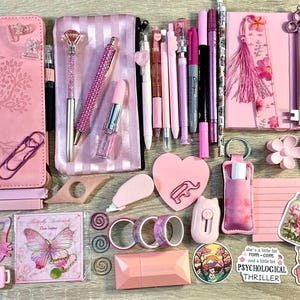 Pu&ograve; includere: Una collezione di articoli di cancelleria rosa che include due quaderni, un astuccio, penne, segnalibri, adesivi, nastro washi, un post-it a forma di cuore, un elastico per capelli e vari accessori da scrivania con motivi floreali e farfalle.
