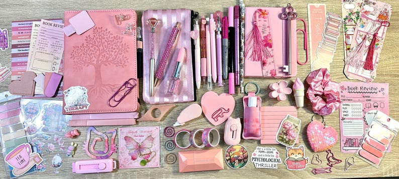 Pu&ograve; includere: Una collezione di articoli di cancelleria rosa che include due quaderni, un astuccio, penne, segnalibri, adesivi, nastro washi, un post-it a forma di cuore, un elastico per capelli e vari accessori da scrivania con motivi floreali e farfalle.
