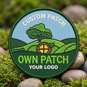 May include: A circular embroidered patch featuring a light blue sky and green rolling hills. A green tree stands above a round brown door. The text reads CUSTOM PATCH at the top, OWN PATCH in the center, and YOUR LOGO at the bottom in white.