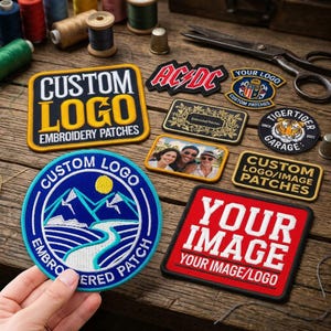 May include: A collection of embroidered patches on a wooden surface, including a large rectangular patch reading CUSTOM LOGO EMBROIDERY PATCHES, a circular patch with a mountain landscape, a red patch reading YOUR IMAGE, and various smaller logo patches.