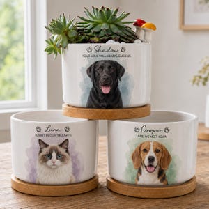 May include: Three white ceramic cylindrical planters with wooden bases. Each features a pet portrait, a name, and a memorial phrase. One shows a black Labrador named Shadow, one a cat named Luna, and one a beagle named Cooper with a succulent.