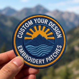 May include: A circular embroidered patch featuring a dark blue background with a yellow sun rising over a dark blue mountain peak and light blue waves. The text CUSTOM YOUR DESIGN EMBROIDERY PATCHES is stitched in white around the border.