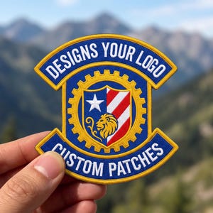 May include: A blue, yellow, red, and white embroidered patch featuring a central gear shape, a shield with a lion head, a white star, and red and white stripes. The text DESIGNS YOUR LOGO is at the top and CUSTOM PATCHES is at the bottom.