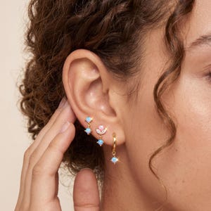 Könnte beinhalten: Ein Set aus drei goldfarbenen Ohrringen mit schillernden blauen Opalsteinen. Ein Ohrring ist ein kleiner Creolen-Ohrring mit einem hängenden Opal, ein weiterer ist ein Stecker mit zwei Opalen und der dritte ist ein halbmondförmiger Stecker.