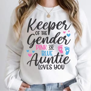 May include: White sweatshirt with the text "Keeper of the Gender Pink or Blue Auntie Loves You" in black script. Pink and blue hearts and footprints accent the design, perfect for a gender reveal.