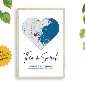 Puede incluir: Impresión enmarcada con un mapa en forma de corazón, dividido en azul y gris, con un corazón rojo que marca una ubicación. Los nombres "Theo & Sarah" están escritos en cursiva debajo del mapa, con la ubicación y la fecha debajo.
