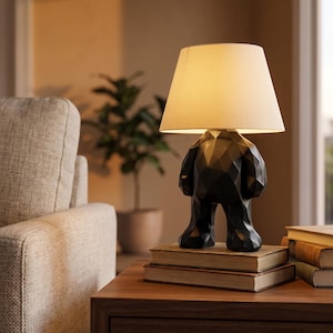 May include: A table lamp featuring a black, faceted, geometric figure base shaped like a stylized character with arms and legs. The lamp is topped with a simple, off-white, conical fabric lampshade that emits a warm, soft glow from within.