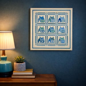 May include: A square wall art piece featuring a grid of nine blue and teal house illustrations. The houses have varying roof and window designs. The artwork is framed with a blue and white border, creating a cohesive and decorative piece.