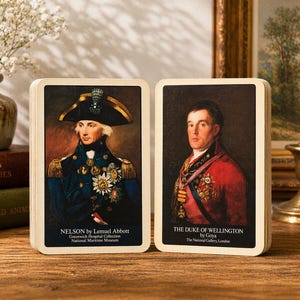 Könnte beinhalten: Zwei Spielkarten mit Porträts historischer Persönlichkeiten. Eine Karte zeigt Nelson von Lemuel Abbott, die andere zeigt den Herzog von Wellington von Goya. Die Karten haben unten Text, der den Künstler und das Museum identifiziert.