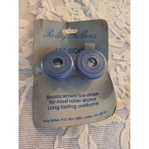 Könnte beinhalten: Ein Paar blaue Reilly Rollers Zehenstopper für Rollschuhe, verpackt auf einer Pappunterlage. Die Verpackung enthält den Text 'Reilly Rollers', 'TOE-STOPS' und 'Replacement toe-stops for most roller skates. Long lasting urethane'.