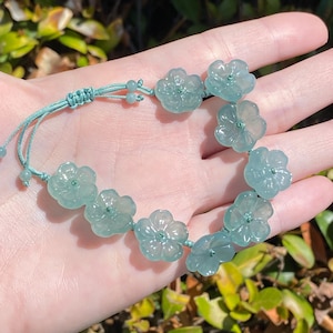 Könnte beinhalten: Ein Armband mit neun durchscheinenden, hellgrünen, blumenförmigen Schnitzperlen, die auf einer passenden hellgrünen Kordel aufgereiht sind. Das Armband verfügt über einen verstellbaren Schiebeknotenverschluss mit zwei kleinen grünen Perlen an den Enden.