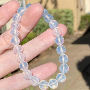 May include: A stretch bracelet composed of smooth, round, translucent white beads with a subtle opalescent sheen. The beads are uniform in size and strung together in a circular loop, reflecting light with a soft, milky glow across their surfaces.