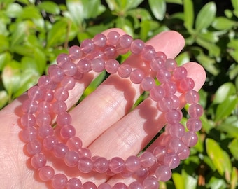 Puede incluir: Una pulsera de múltiples hilos compuesta por cuentas rosas translúcidas, lisas y redondas. Las cuentas tienen un acabado pulido y una forma esférica consistente, ensartadas para formar un bucle circular continuo que refleja la luz.