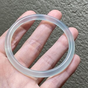 May include: A smooth, translucent, pale light blue bangle bracelet with a polished finish. The circular accessory features a consistent, rounded profile and a clear, icy appearance that allows light to pass through the material evenly.