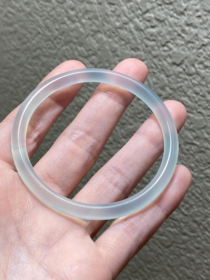 May include: A smooth, translucent, pale light blue bangle bracelet with a polished finish. The circular accessory features a consistent, rounded profile and a clear, icy appearance that allows light to pass through the material evenly.