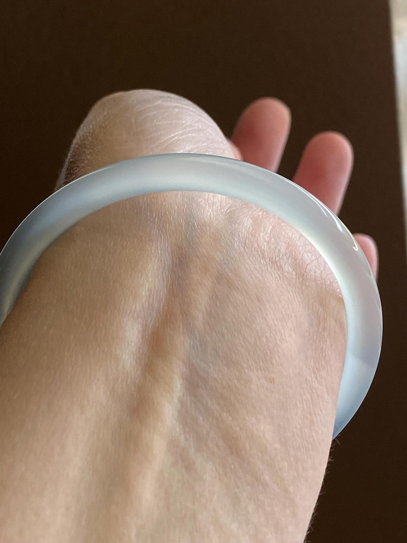May include: A smooth, translucent white bangle bracelet with a rounded profile. The material appears to have a soft, milky quality with subtle light diffusion throughout the circular band, creating a clean and simple aesthetic for the wrist.