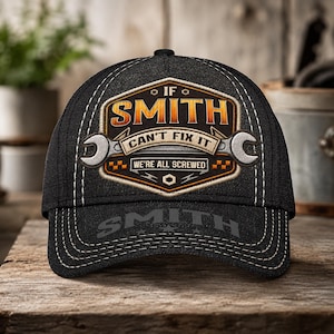 May include: Black baseball cap with white stitching and the name "SMITH" embroidered on the bill. The cap features a patch with the text "IF SMITH CAN'T FIX IT WE'RE ALL SCREWED" and wrench graphics.