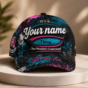May include: A black baseball cap featuring a vibrant paint-splatter design in shades of blue and pink. The front displays the text "It's a Your name Thing... You Wouldn't Understand" and "Acosta" in pink script. A circular "H" logo is on the side.