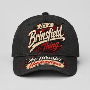 May include: A dark gray baseball cap with the text "It's a Brinsfield Thing... You Wouldn't Understand" in white and red lettering. The cap has a curved brim and a button on top.