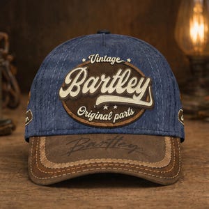 May include: A blue baseball cap with a brown leather bill. The cap features the text "Vintage Bartley Original Parts" in a circular patch. The bill has the name "Bartley" printed on it. The cap is made of a durable material.