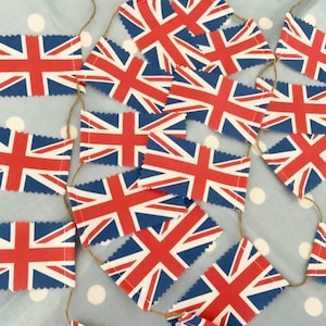 May include: A string of bunting with red, white, and blue Union Jack flags. The flags are sewn together with white thread and strung on a twine.