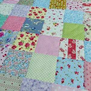 May include: A patchwork quilt featuring a mix of floral and patterned fabrics in pastel shades. The quilt is composed of squares in pink, blue, yellow, and green, creating a charming and colourful design. The quilt is likely handmade.