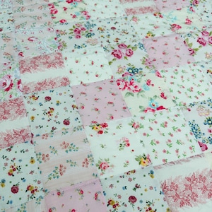 May include: A patchwork quilt with a mix of floral fabrics in pink, red, and cream. The quilt is composed of numerous fabric squares, each with a different floral design, creating a charming and cosy aesthetic.