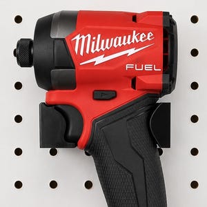 May include: A red and black Milwaukee FUEL impact driver with a black handle and battery pack. The tool is mounted on a white pegboard. The battery pack reads M18 REDLITHIUM XC5.0.