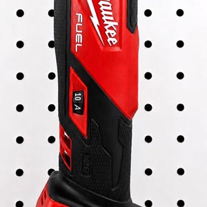 May include: A red and black Milwaukee FUEL cordless right angle drill. The drill is mounted on a white pegboard. The drill has the Milwaukee logo and the text "10 A" and "M18 REDLITHIUM XC5.0" printed on it.