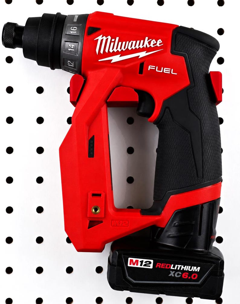 May include: A red and black Milwaukee FUEL M12 cordless screwdriver. The tool has a black handle and a battery pack labeled "M12 REDLITHIUM XC6.0". The Milwaukee logo is visible in white. The screwdriver is mounted on a white pegboard.