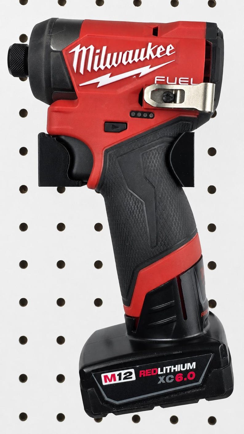 May include: A red and black Milwaukee FUEL impact driver. The tool has a black grip, a red body, and the Milwaukee logo in white. The battery pack is labeled M12 REDLITHIUM XC 6.0. It is mounted on a black pegboard.