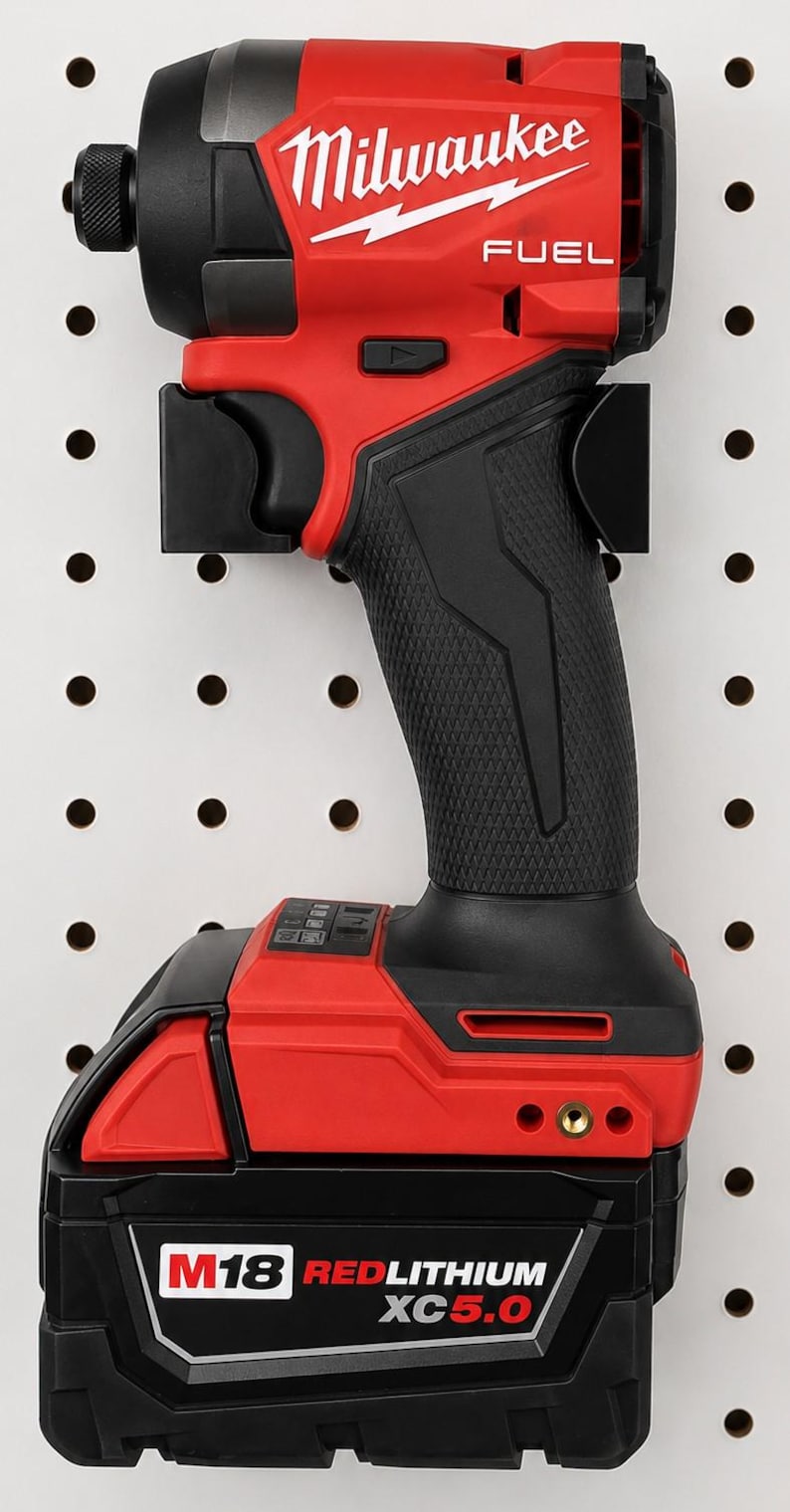 May include: A red and black Milwaukee FUEL impact driver with a black handle and battery pack. The tool is mounted on a white pegboard. The battery pack reads M18 REDLITHIUM XC5.0.