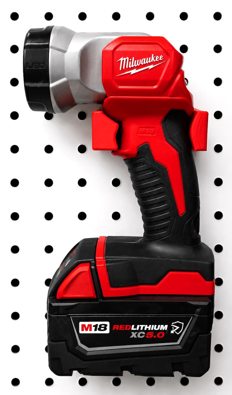 May include: A red and black Milwaukee M18 LED work light with a black handle and battery pack. The light has a silver head and the Milwaukee logo in white. The battery pack is labeled M18 REDLITHIUM XC5.0.