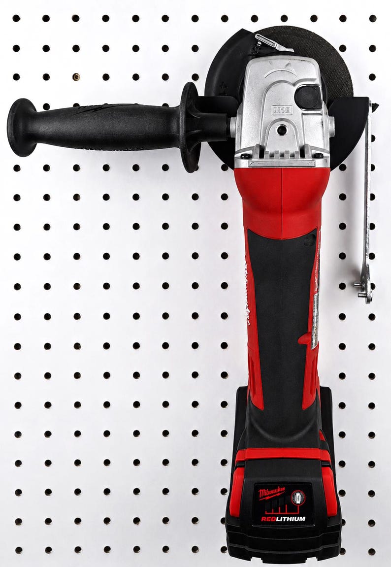 May include: A red and black cordless angle grinder with a black handle and a silver head. The grinder is mounted on a white pegboard. The brand name "Milwaukee" is visible on the tool.